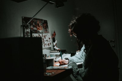 穿着灰色针织运动衫的女人在书桌上写字的微光摄影